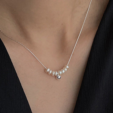 Pearl necklace worn by a person in a black garment against a neutral background