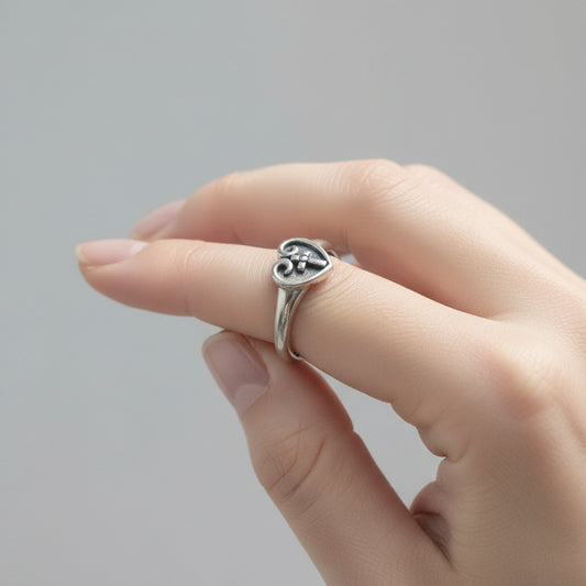 Silver ring with heart-shaped design and cross on a white background