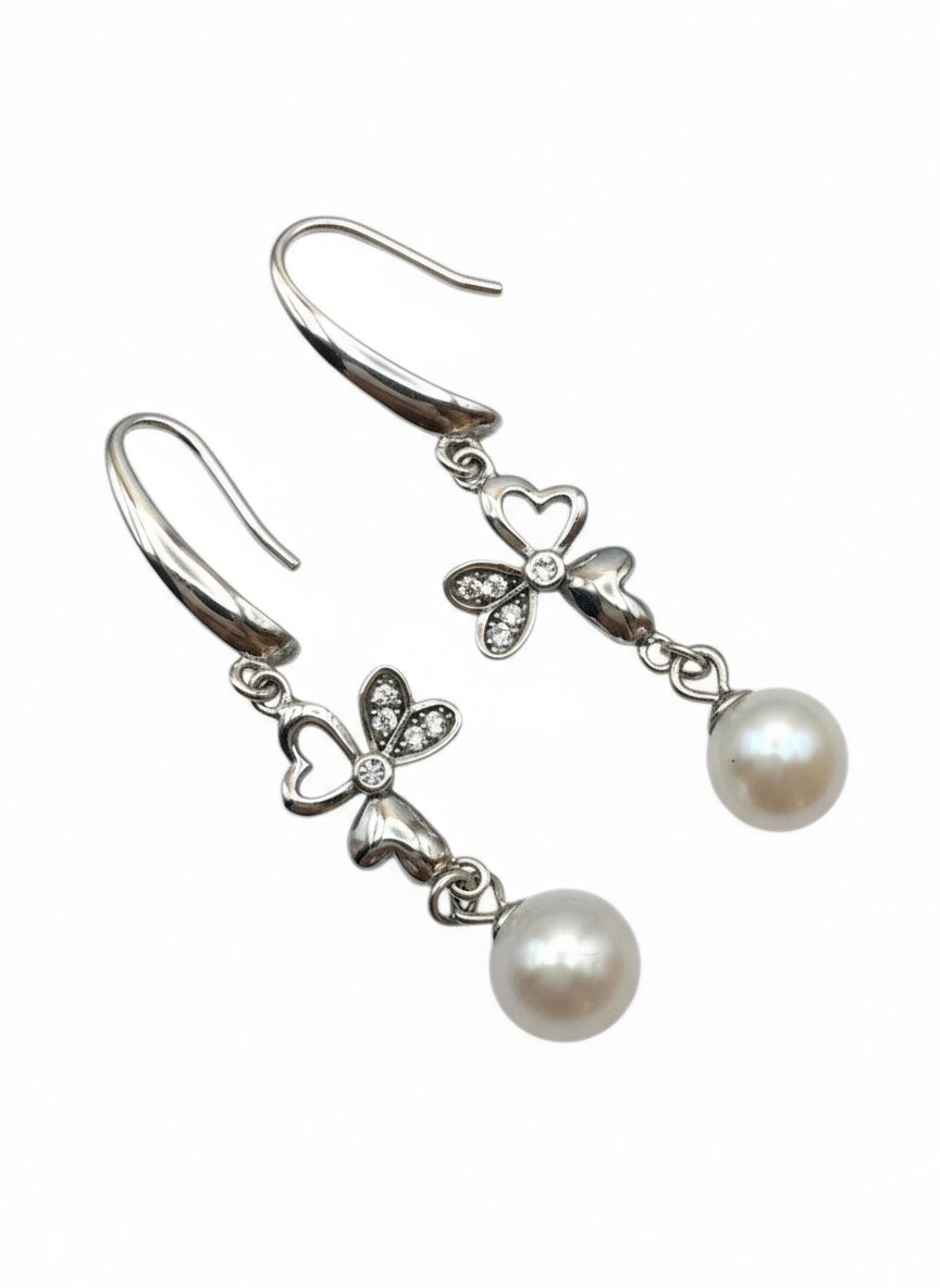Pearl earrings with silver bow designs on a white background