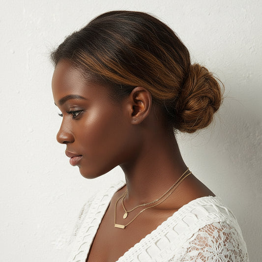 Woman with styled hair and gold necklaces against a plain background