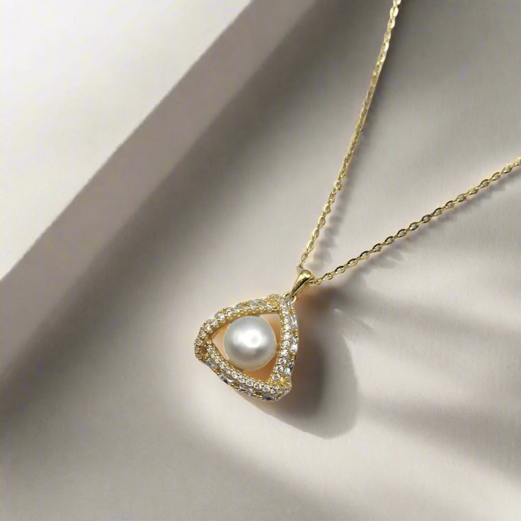 Gold necklace with a heart-shaped pendant featuring a pearl on a white background
