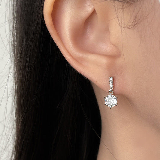 Close-up of an ear wearing a diamond earring with a neutral background