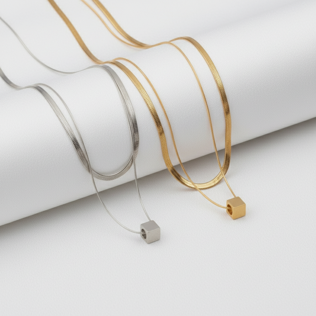 Two gold necklaces with square pendants on a white background