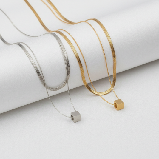 Two gold necklaces with square pendants on a white background