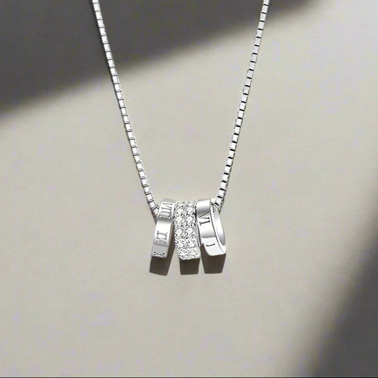 Silver necklace with three pendant charms on a white background