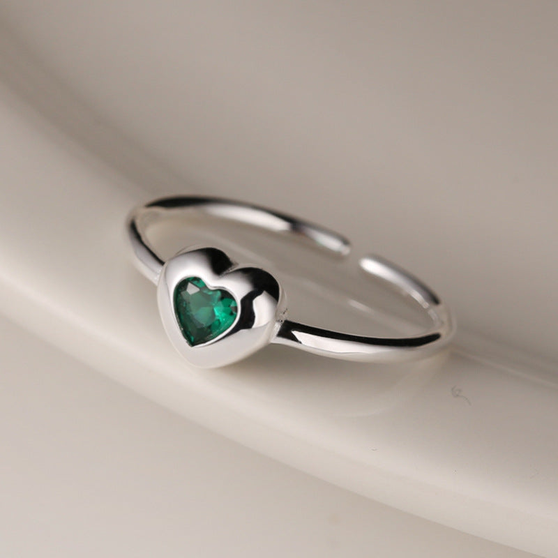 Silver ring with a heart-shaped green gemstone on a neutral background