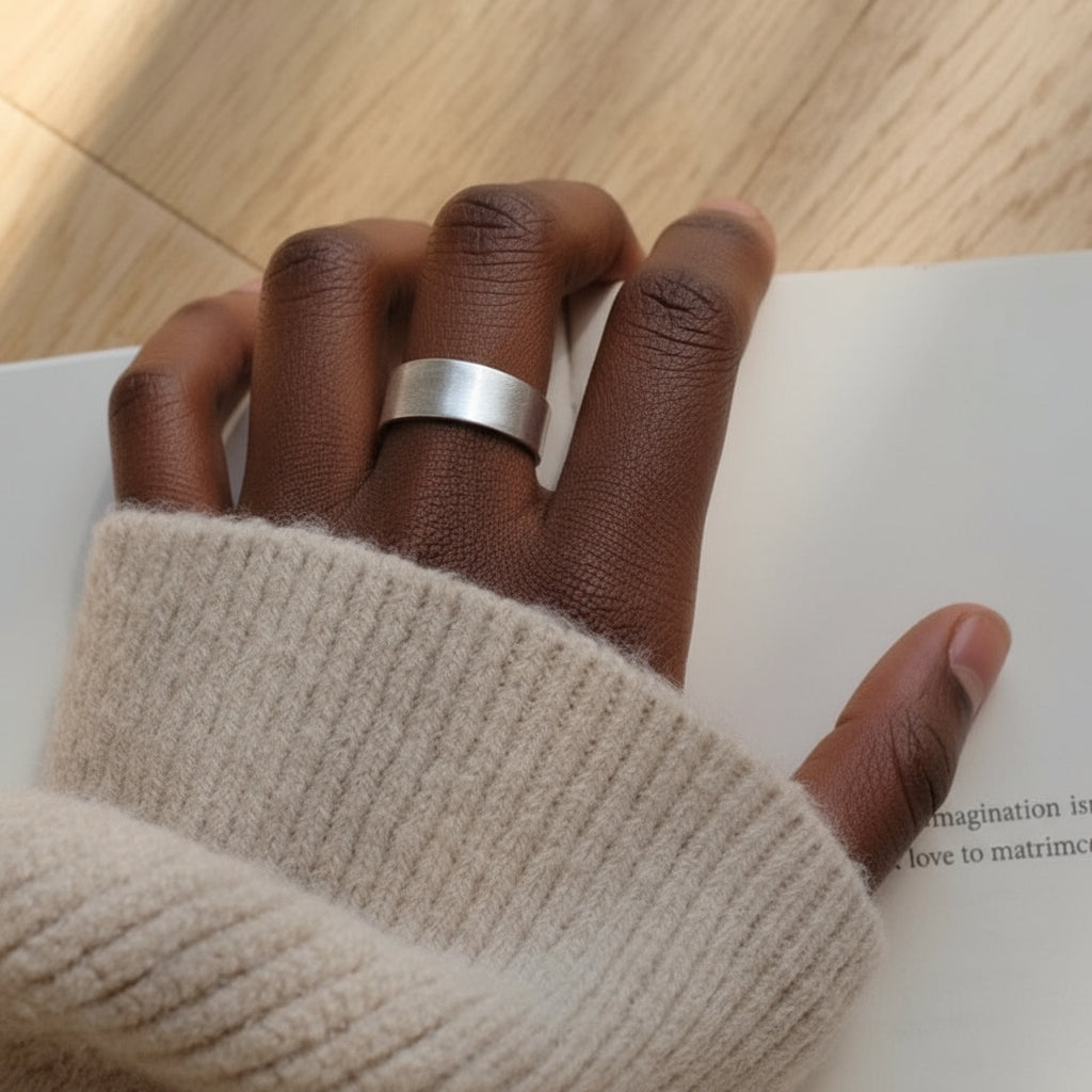 Hand wearing a silver ring on a wooden surface