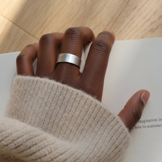 Hand wearing a silver ring on a wooden surface