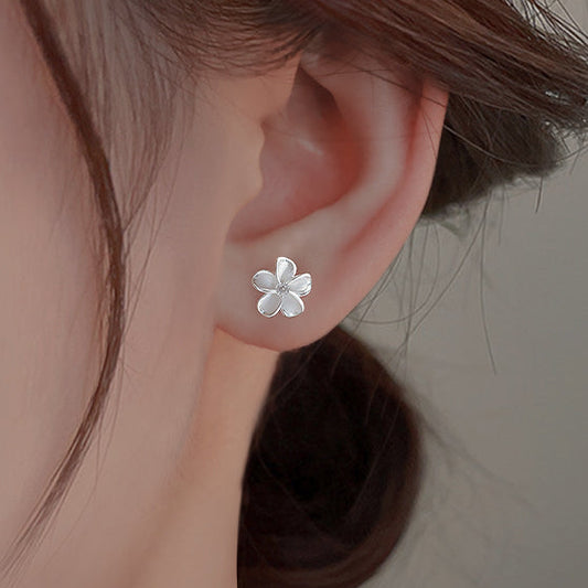 Silver flower-shaped earring worn by a person with a neutral background