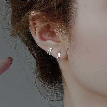 Person wearing silver earrings with a hand pointing towards them against a gray background