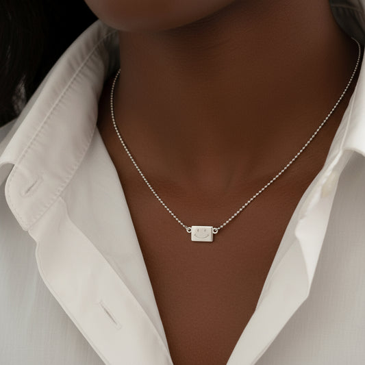 Silver necklace with a square pendant on a person wearing a white blouse.