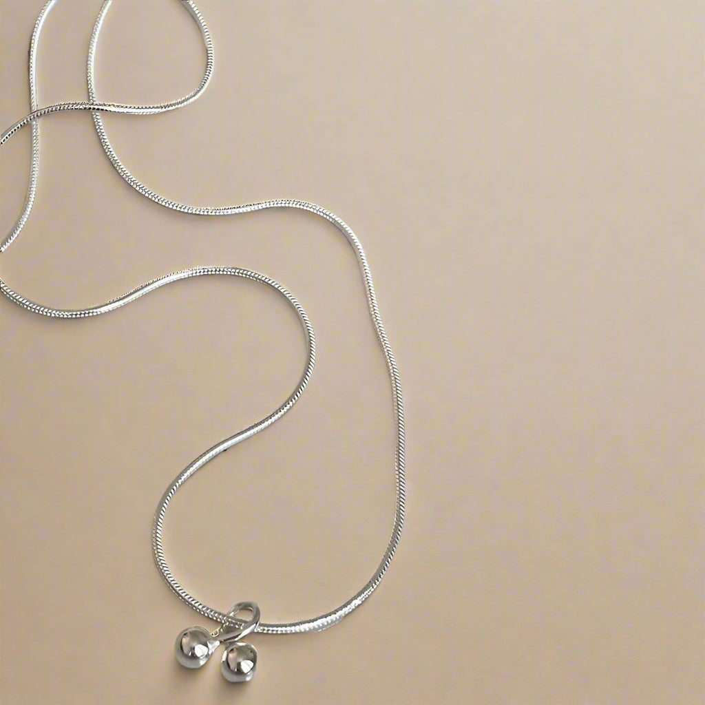 Silver necklace with two small round pendants on a speckled ceramic plate.