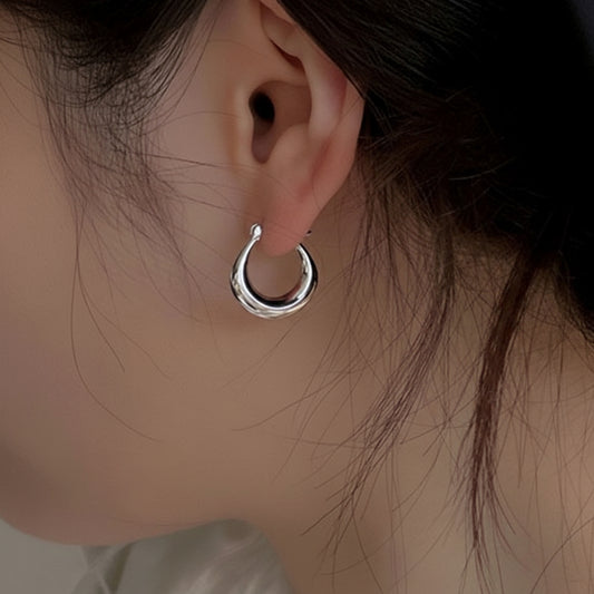 Close-up of a person wearing a silver hoop earring with a blurred background