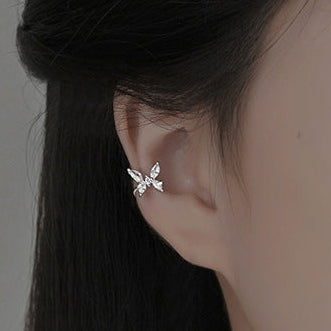 Close-up of a person wearing a silver butterfly earring with a plain background