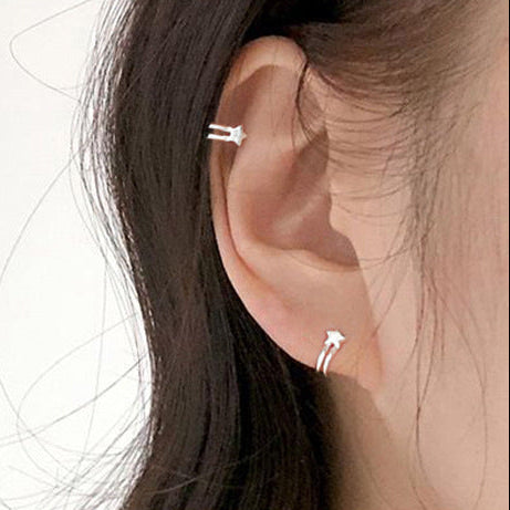 Close-up of an ear wearing two silver earrings with a plain background