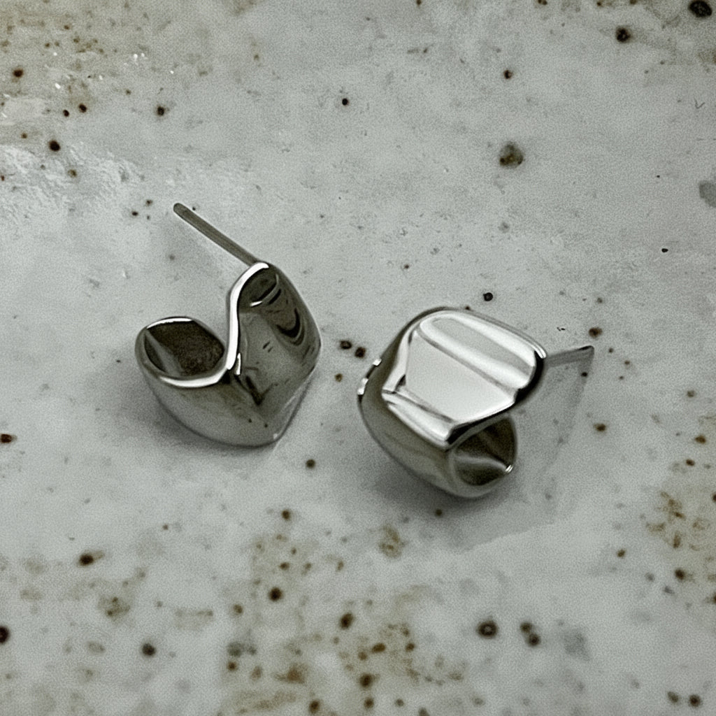 Silver geometric stud earrings on a textured surface