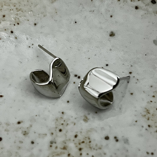 Silver geometric stud earrings on a textured surface