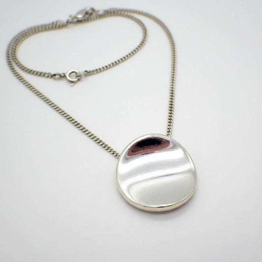 Silver necklace with a round pendant on a light gray background
