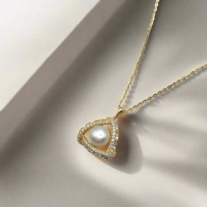 Gold necklace with a heart-shaped pendant featuring a pearl on a white background