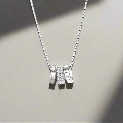 Silver necklace with three pendant charms on a white background