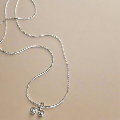 Silver necklace with two small round pendants on a speckled ceramic plate.