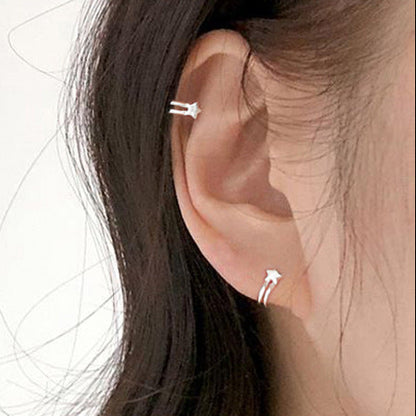 Close-up of an ear wearing two silver earrings with a plain background